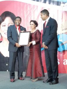Prime Minister Kamla Persad-Bissessar SC, receives an award from Broward County Commissioner, Dale Holness, left, at a Republic Day dinner in South Miami, on Monday night. At right is T&T Consul General, Dr Anil Ramnanan.