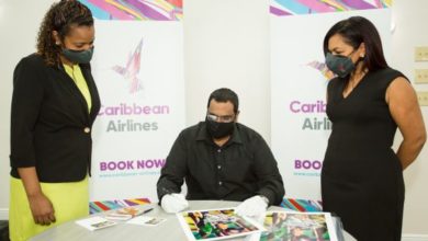 Caribbean Airlines Loyalty Coordinator Gillian Samuel, Photographer Sanjiv Samoaroo signs prints of his work 'Hummingbird Mother with Babies' and Executive Manager Marketing and Loyalty, Alicia Cabrera.