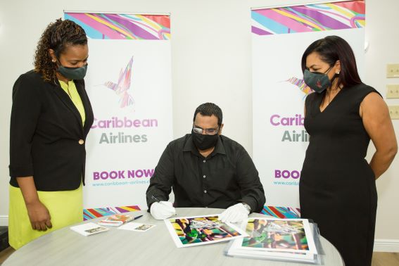 Caribbean Airlines Loyalty Coordinator Gillian Samuel, Photographer Sanjiv Samoaroo signs prints of his work 'Hummingbird Mother with Babies' and Executive Manager Marketing and Loyalty, Alicia Cabrera.